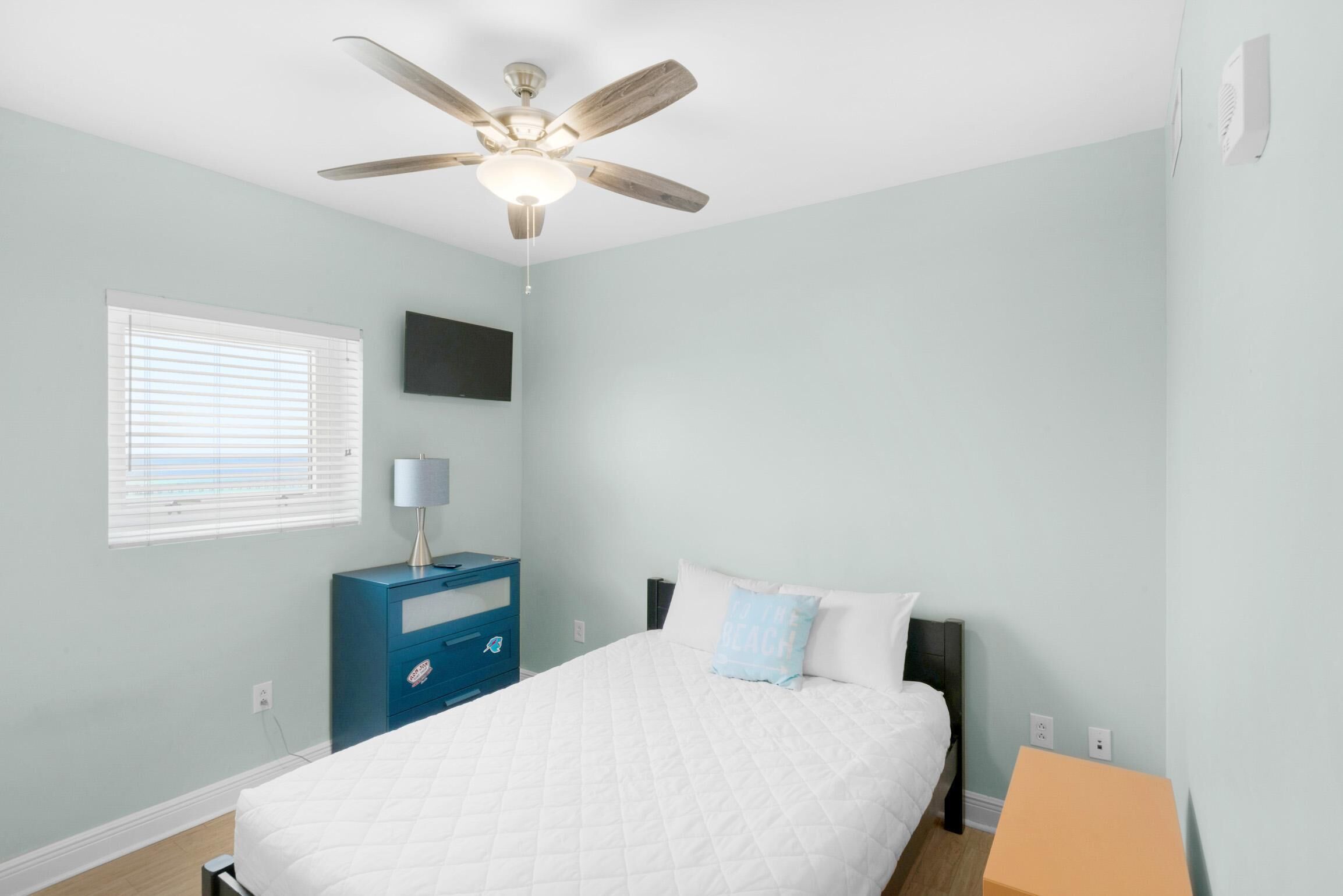 A bedroom with a bed, a ceiling fan, a nightstand, a lamp, and a window with blinds.