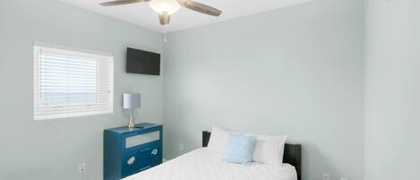 A bedroom with a bed, a ceiling fan, a nightstand, a lamp, and a window with blinds.