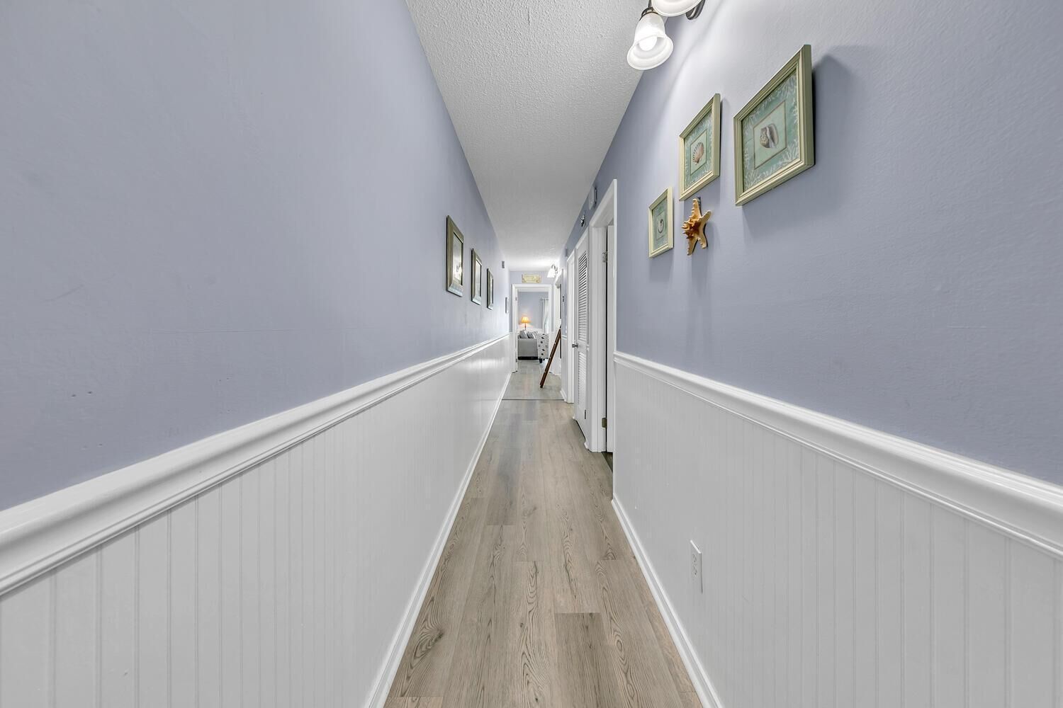 Un couloir aux murs bleu clair, avec des lambris blancs et un plancher en bois.