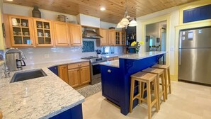 A modern kitchen with wooden cabinets, a granite countertop, a stainless steel refrigerator, and a blue island with stools. - Large Groups! Pine Point Beach 8 BDRM! (Scarborough)