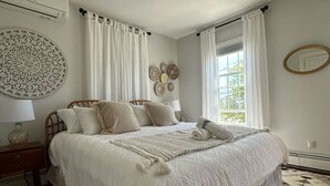 A bedroom with a large bed, white curtains, a round mirror, and a decorative wall piece. - Large Groups! Pine Point Beach 8 BDRM! (Scarborough)