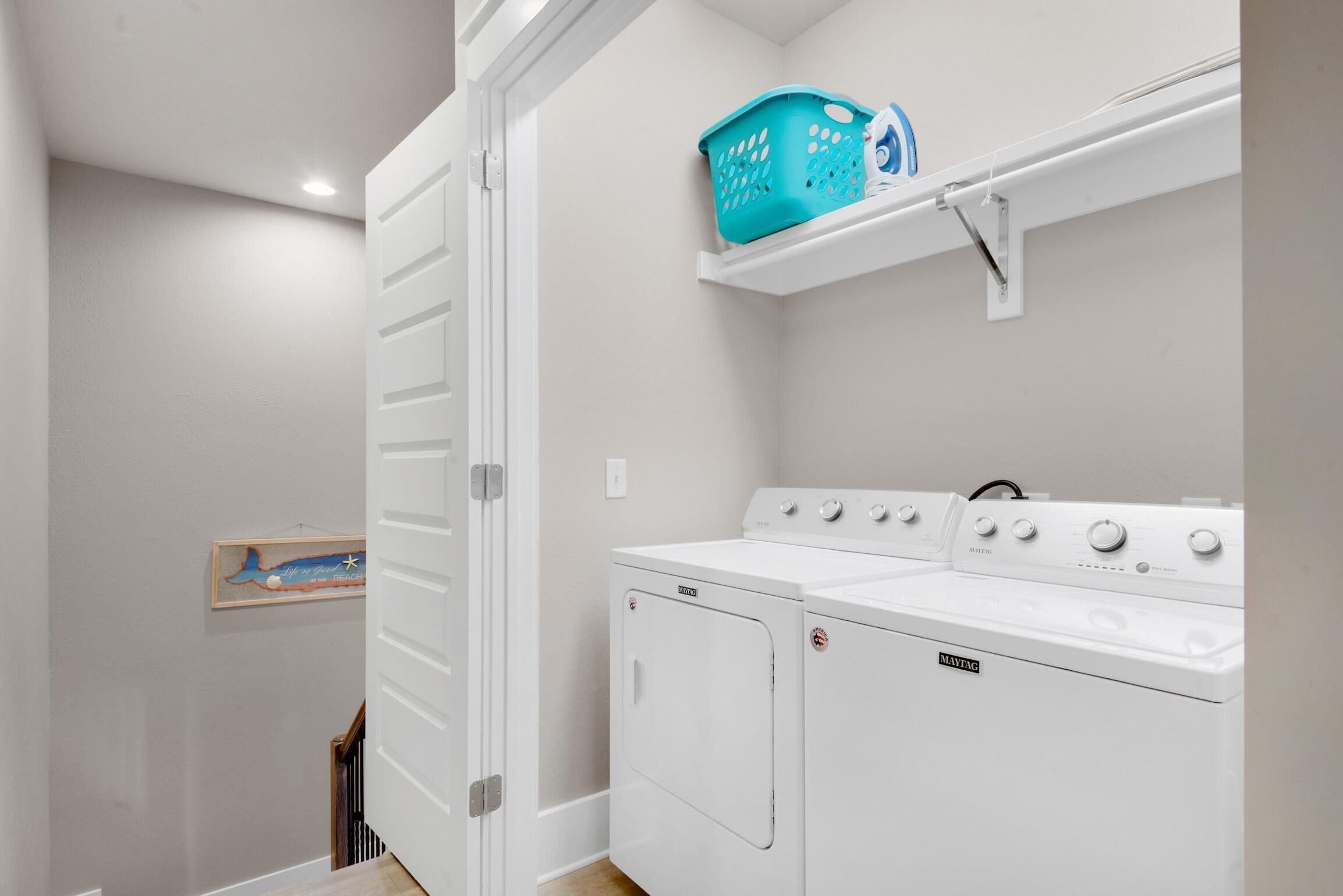 Une buanderie avec un lave-linge et un sèche-linge blancs, un panier bleu posé sur une étagère et une porte en bois.