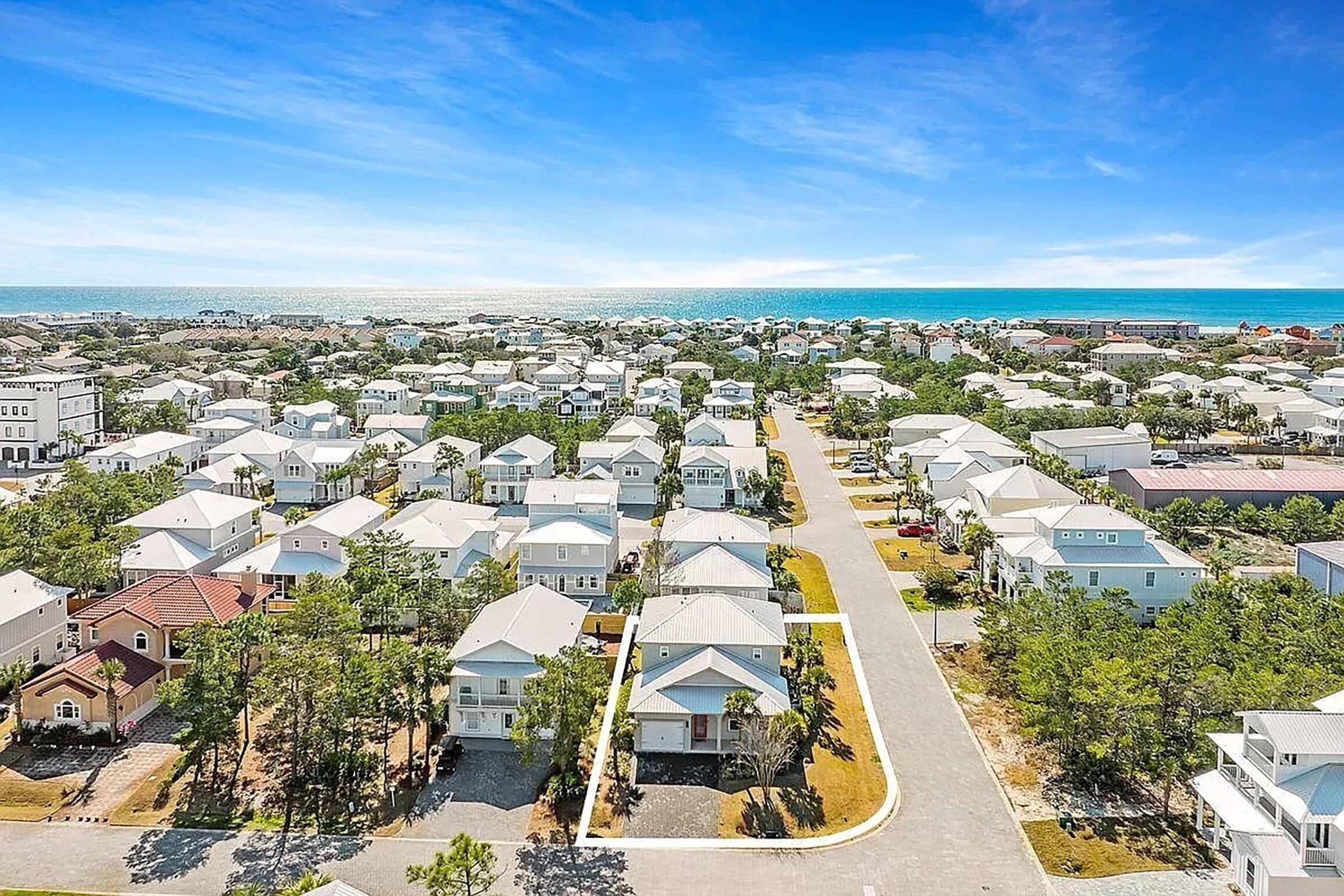 A residential area with houses arranged in rows, a clear road, and a view of the ocean.