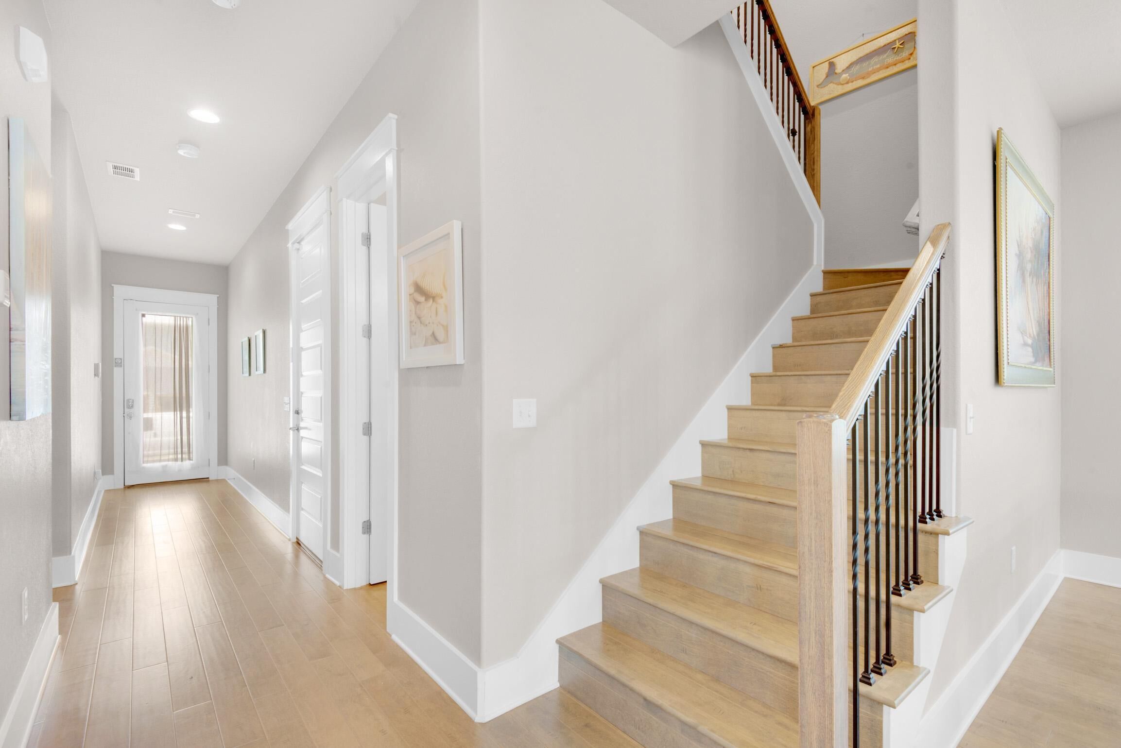A hallway with wooden flooring, white walls, and a wooden staircase with a railing.