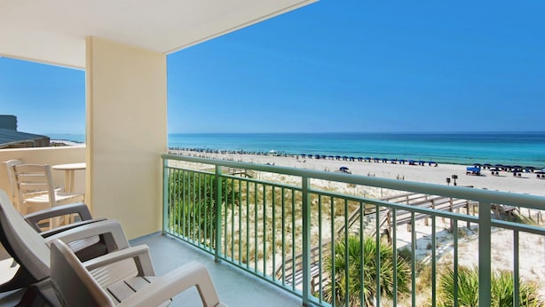 A balcony with white chairs and a view of a beach with people and umbrellas. - Pelican Isle 301 (Fort Walton Beach)