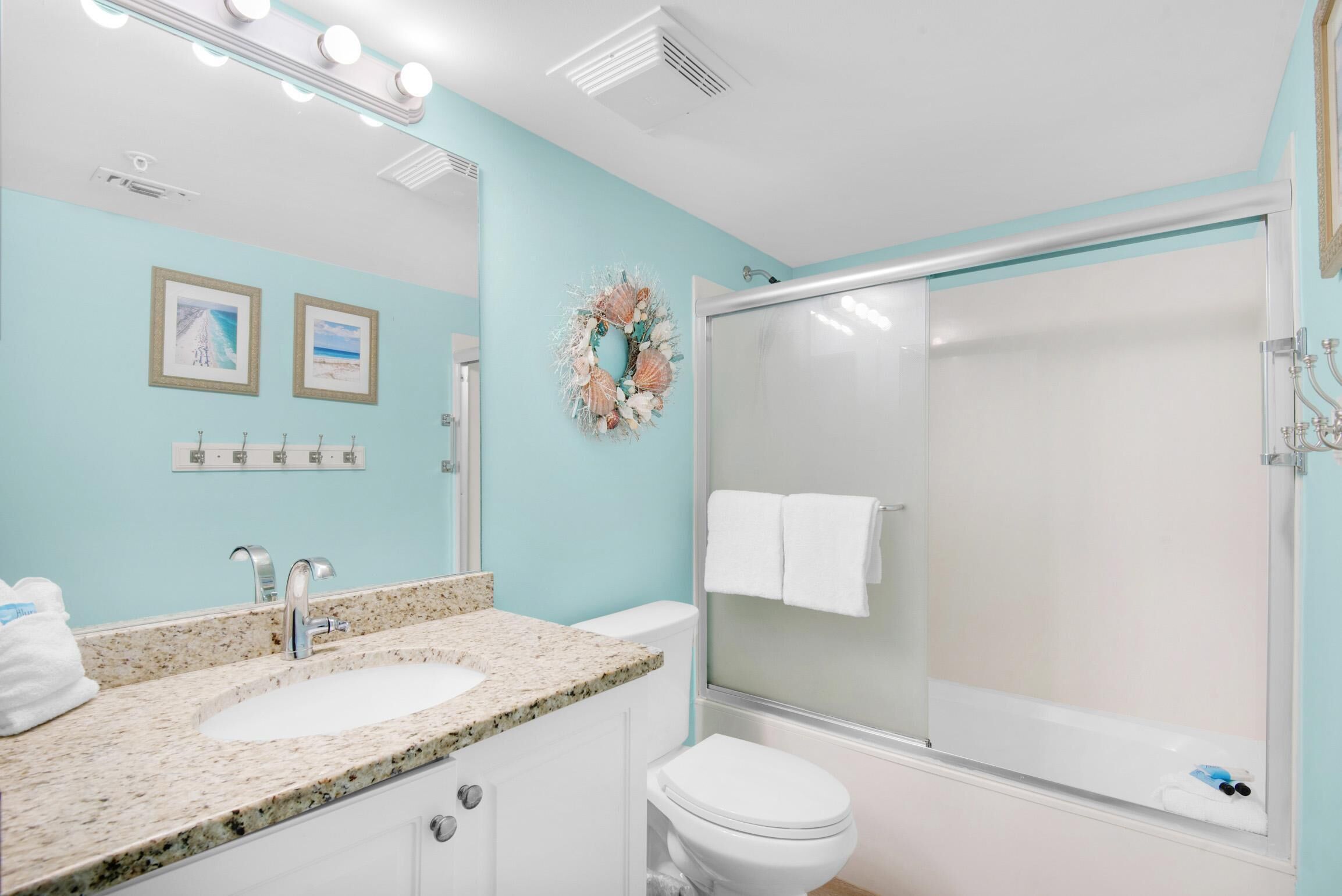 A bathroom with a granite countertop sink, a white toilet, and a glass-enclosed shower.