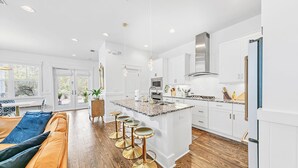 A modern kitchen with white cabinets, a central island with stools, and a wooden floor.