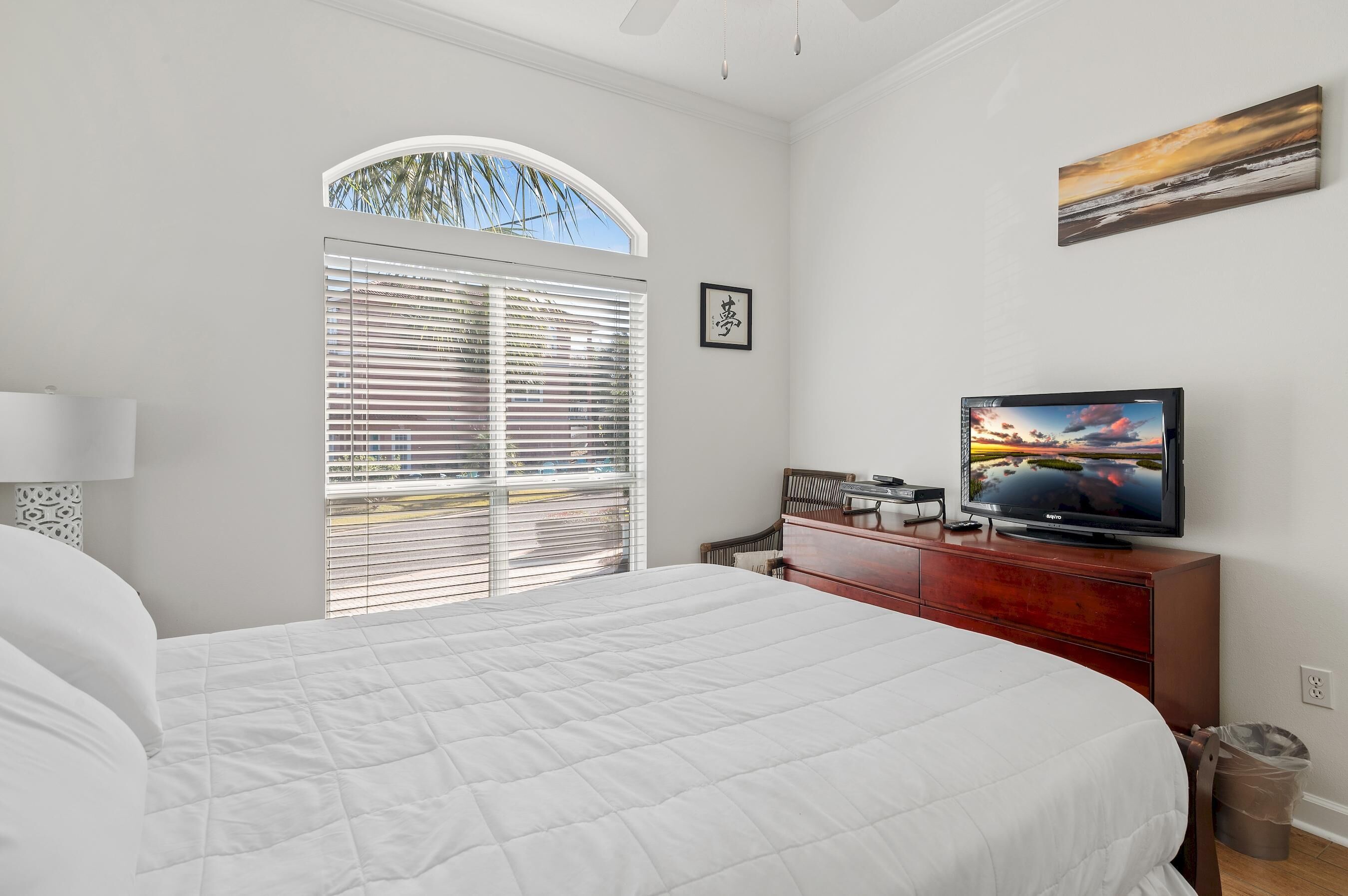 Una camera da letto con un letto grande, una televisione su una cassettiera in legno, una finestra con persiane e un quadro al muro.