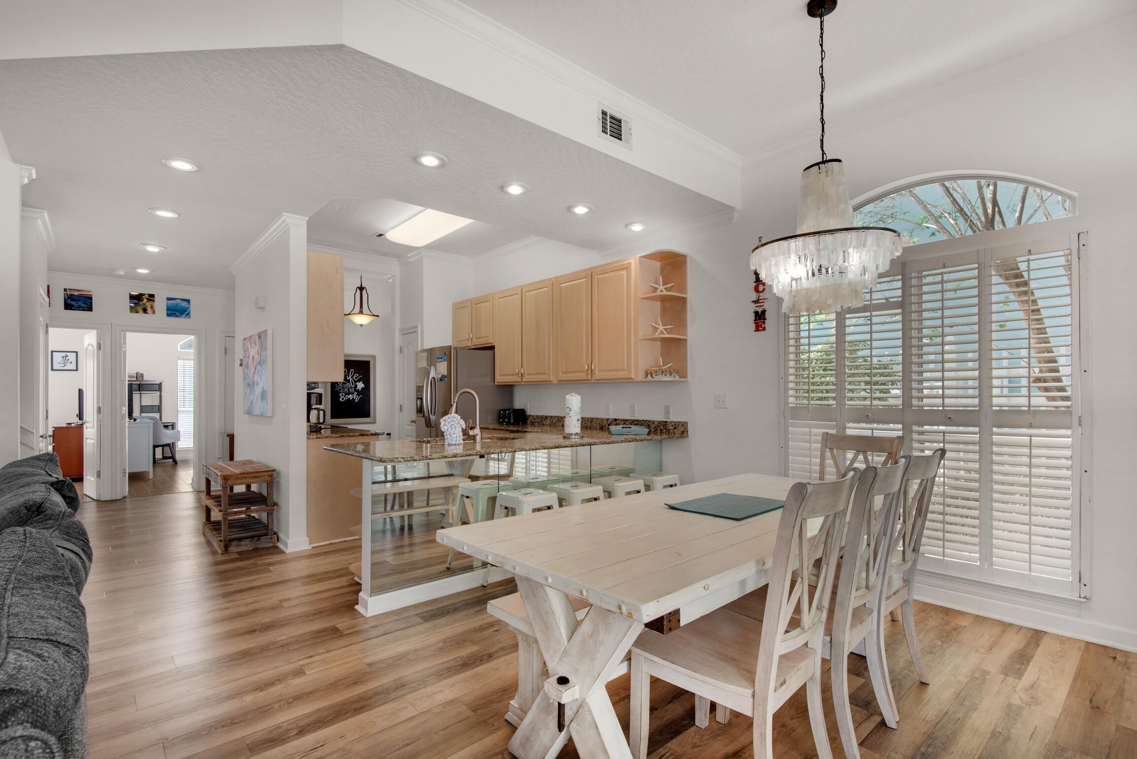 A spacious kitchen with wooden cabinets, a dining area with a white table and chairs, and a large window with shutters.