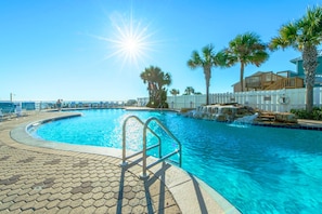 A swimming pool with a sunlit sky, palm trees, and a white fence.