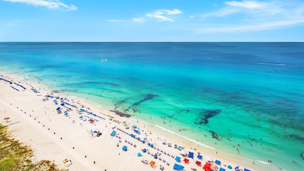 A beach with clear turquoise water, a sandy shore, and numerous umbrellas. - Majestic Beach Towers 1-2113 (Panama City Beach)