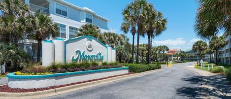 A hotel entrance with a sign, palm trees, and a clear blue sky.