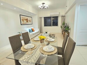 A modern dining area with a glass table, woven placemats, and a sofa in the background.
