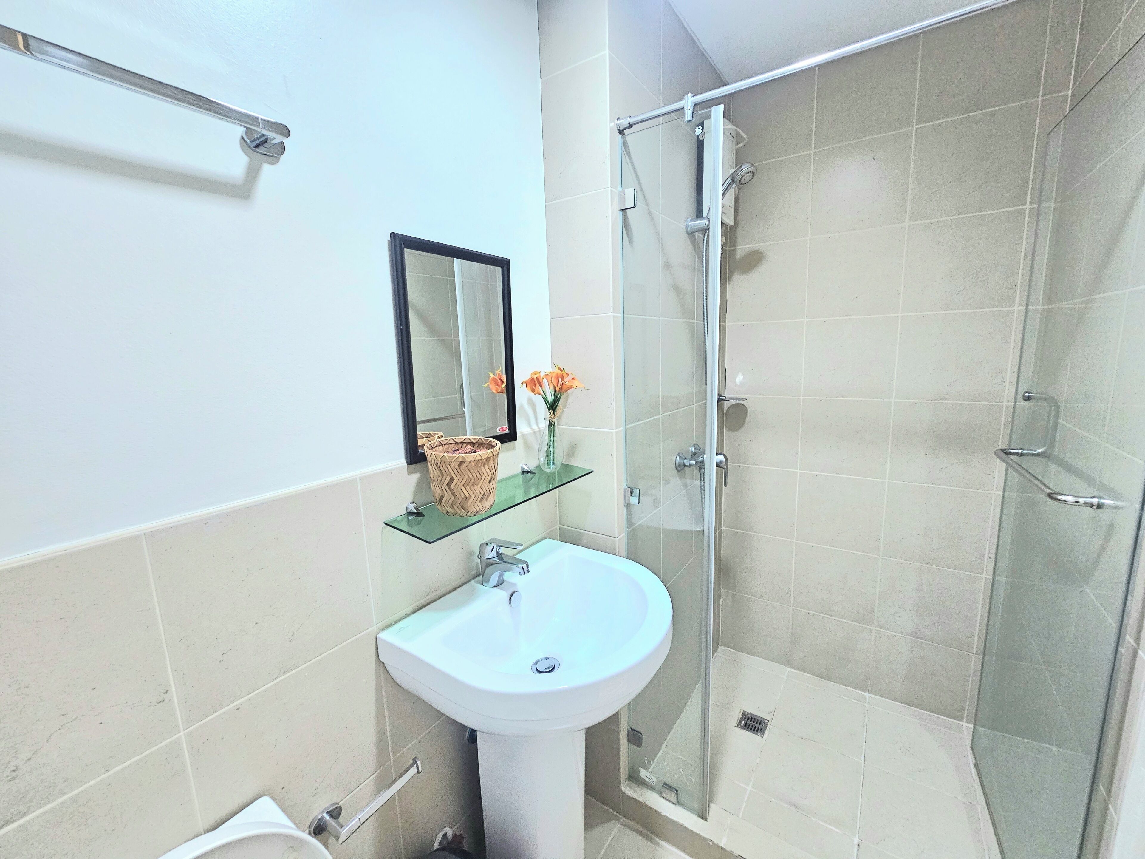 Une salle de bain avec une douche à parois de verre, un lavabo blanc et un miroir agrémenté d'un panier et d'un vase en osier.