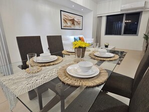 A modern dining area with a glass table, woven placemats, and white tableware. - The Infinity (Taguig)