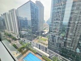 Un edificio de gran altura con fachada de vidrio reflectante, rodeado de otros edificios altos y un área de piscina bajo un cielo despejado.