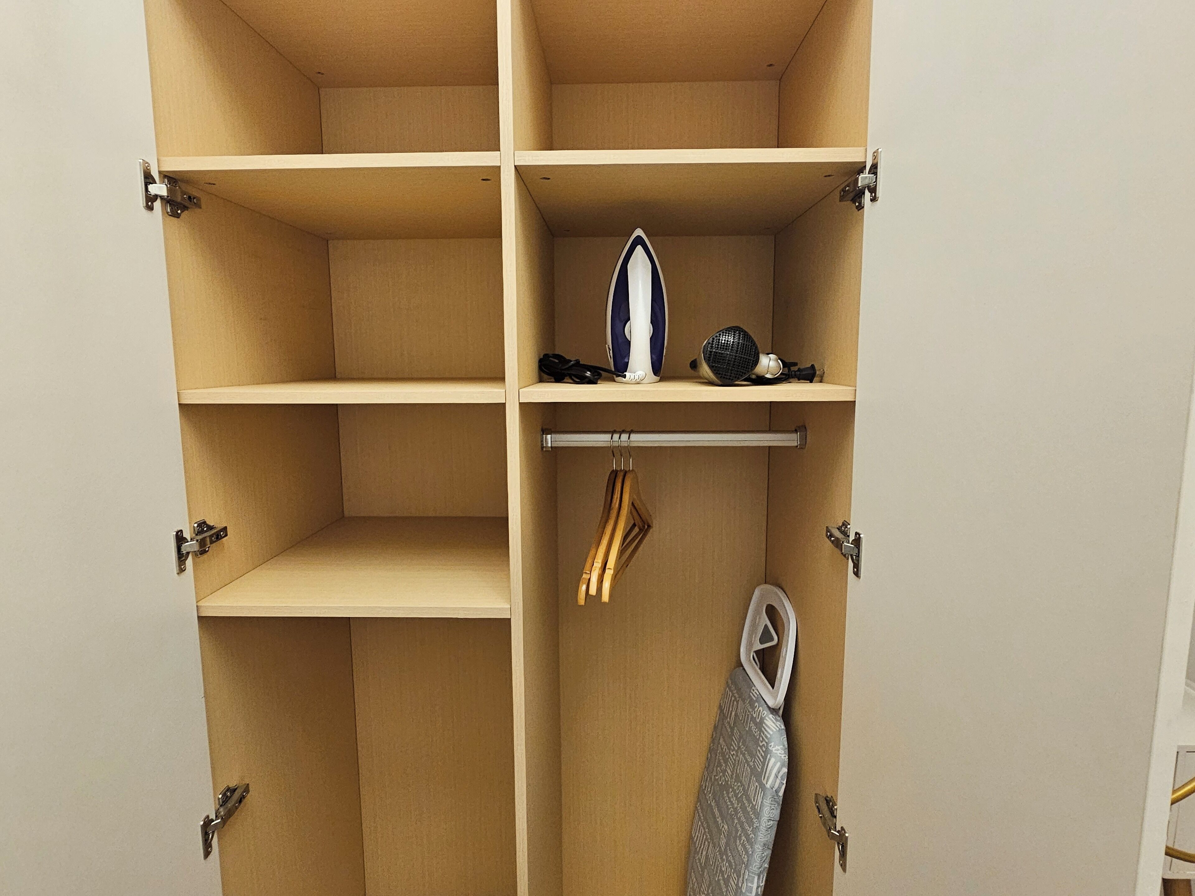 A wardrobe with multiple compartments, a hanging rack, and a shelf with a mirror and a hairdryer.