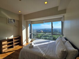 A bedroom with a large window, a bed, a wooden bench, and a ceiling fan.