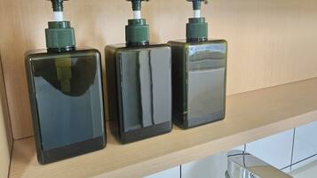 Three black bottles with green pumps on a wooden shelf in a kitchen.
