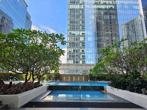 A modern building with a glass facade, a swimming pool, and surrounding greenery.