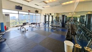 Et rummeligt fitnessrum med forskellig træningsudstyr, store vinduer og et højt til loftet.