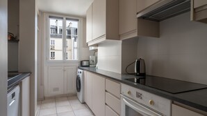 A compact kitchen with a washing machine, a coffee maker, and a stove. - Appartement Apalta - Welkeys (Paris)