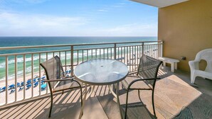 Ein Balkon mit Glastisch und Stühlen, der auf einen Strand mit Sonnenschirmen und den Ozean blickt.
