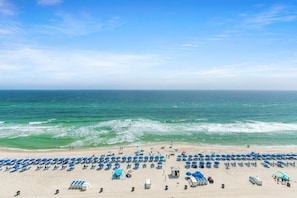 Een strand met rijen blauwe parasols en ligbedden, een klein strandhutje en een toren voor de strandwacht.