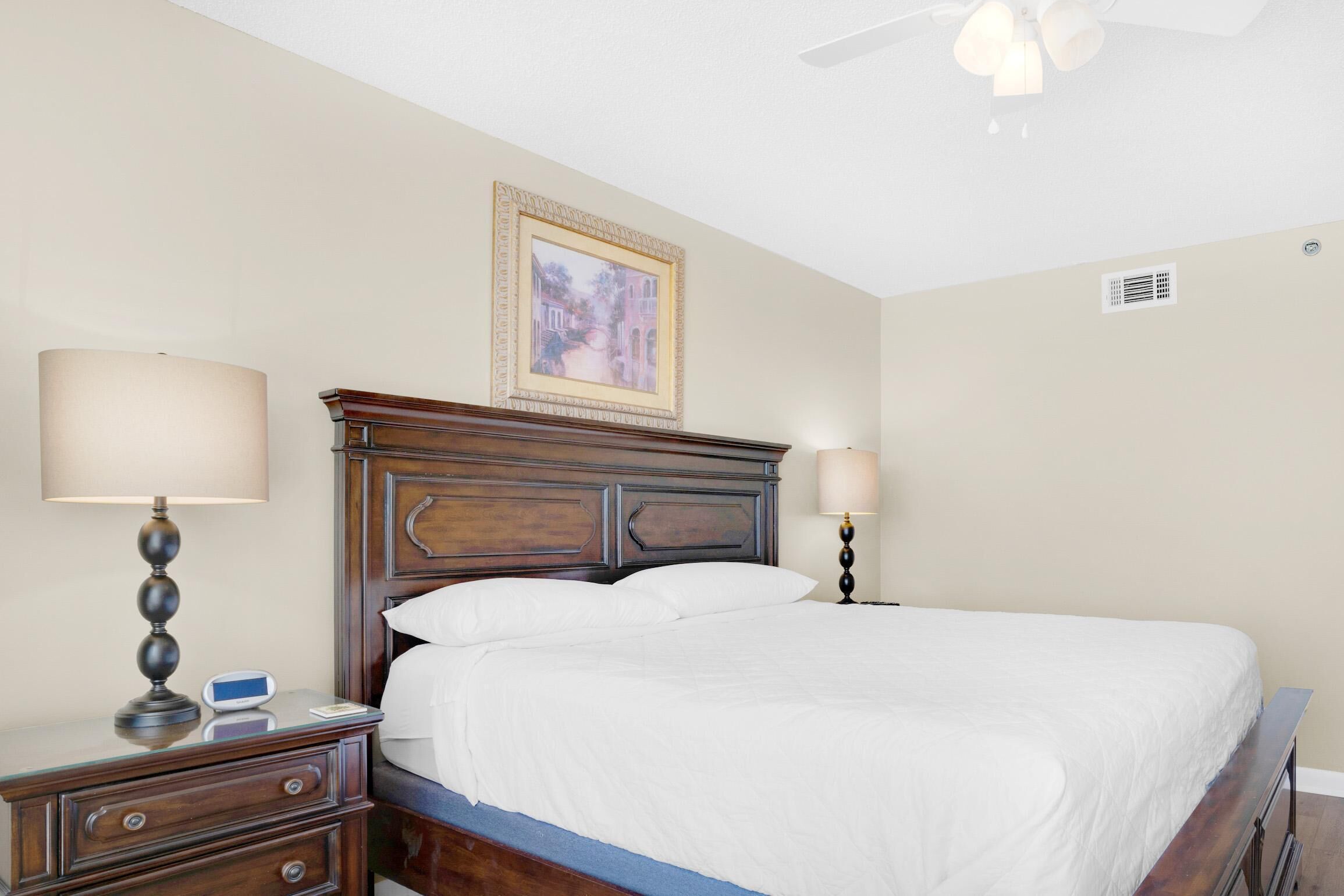 A neatly made bed with a wooden headboard, two bedside lamps, and a digital clock on a bedside table.