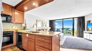 A modern kitchen with wooden cabinets, a granite countertop, and a built-in oven. - Edgewater Tower 1-305 (Panama City Beach)