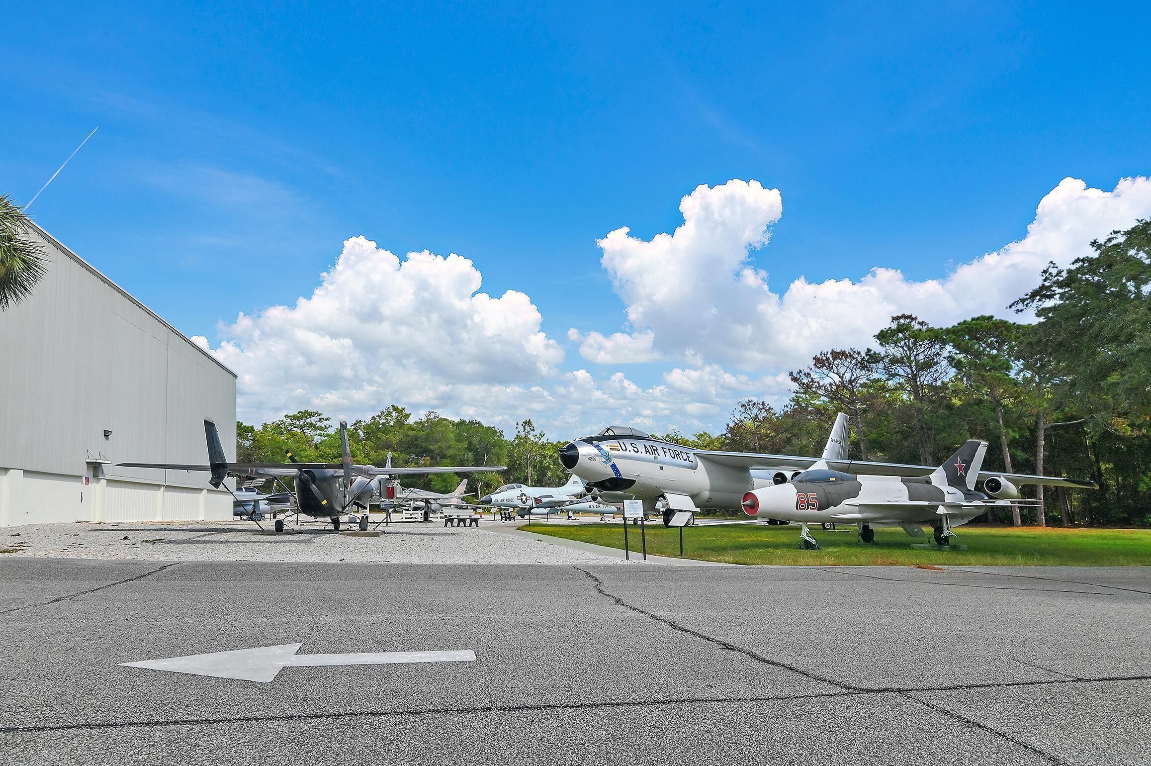 Ein ausstellendes Militärflugzeug vor blauem Himmel und Bäumen im Hintergrund.