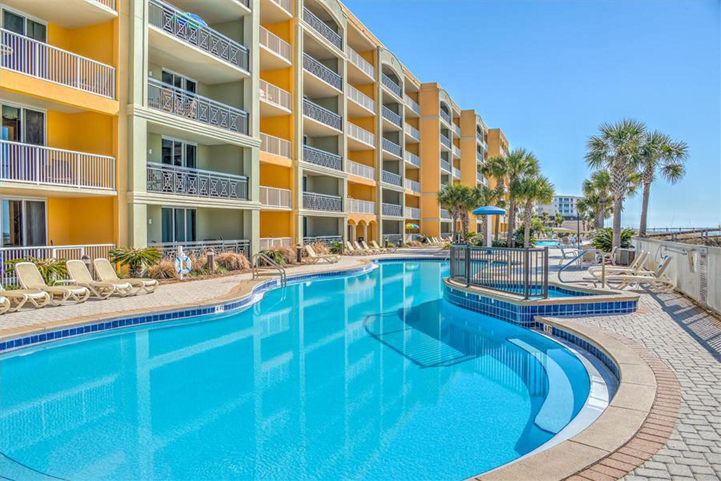 A hotel with a large pool, multiple balconies, and palm trees.