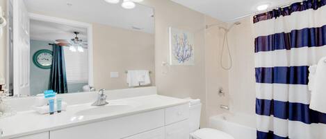 A bathroom with a white sink, mirror, and toilet. There is a shower curtain and a towel rack.