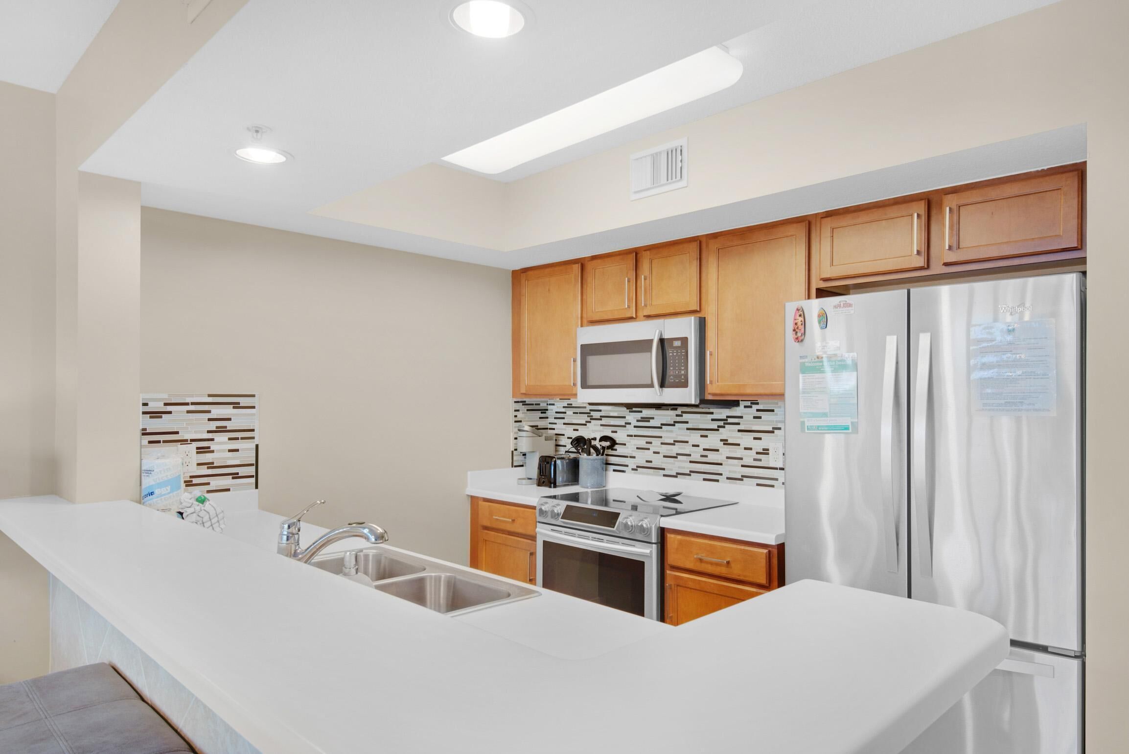 A modern kitchen with wooden cabinets, stainless steel appliances, and a white countertop.