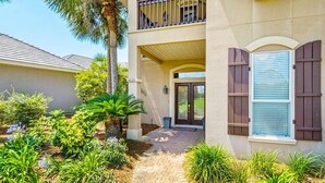 A two-story house with a paved entrance, a balcony, and a well-maintained garden with various plants and a palm tree. - Ocean Pearl (Destin)