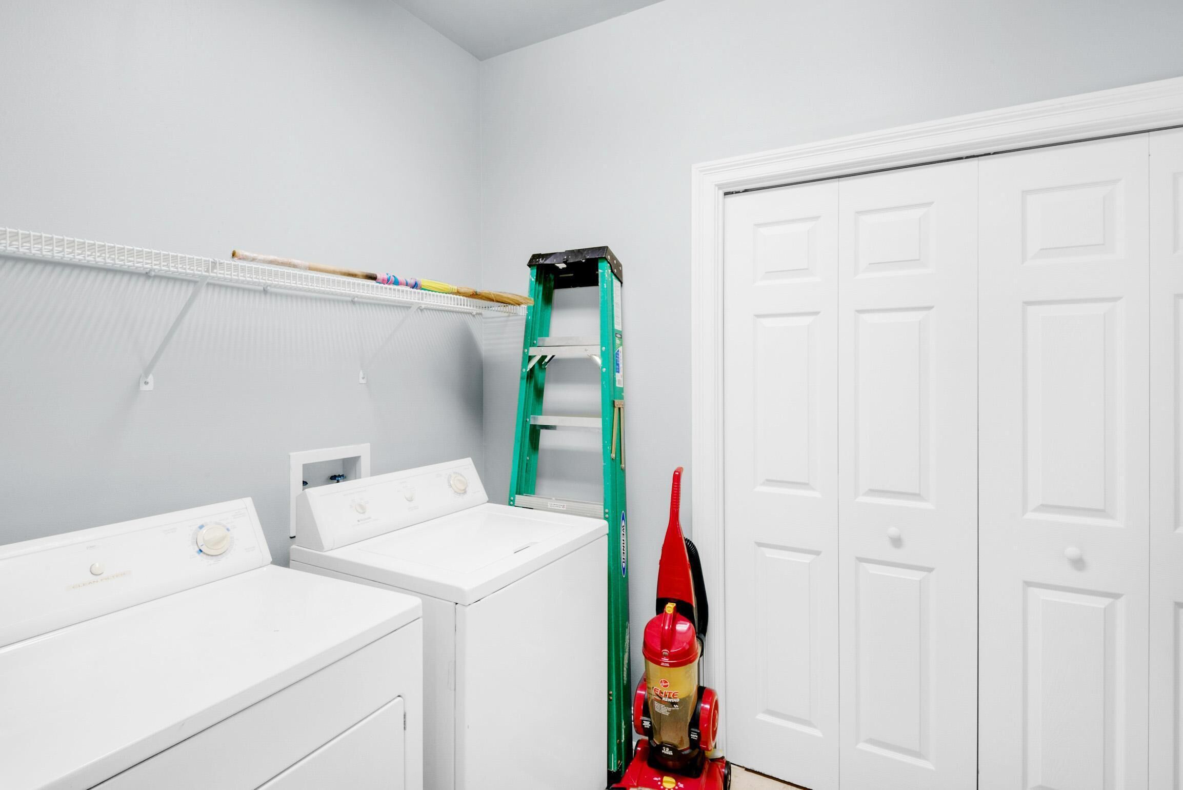 A laundry room with stacked laundry, a green ladder, and a red fire extinguisher.