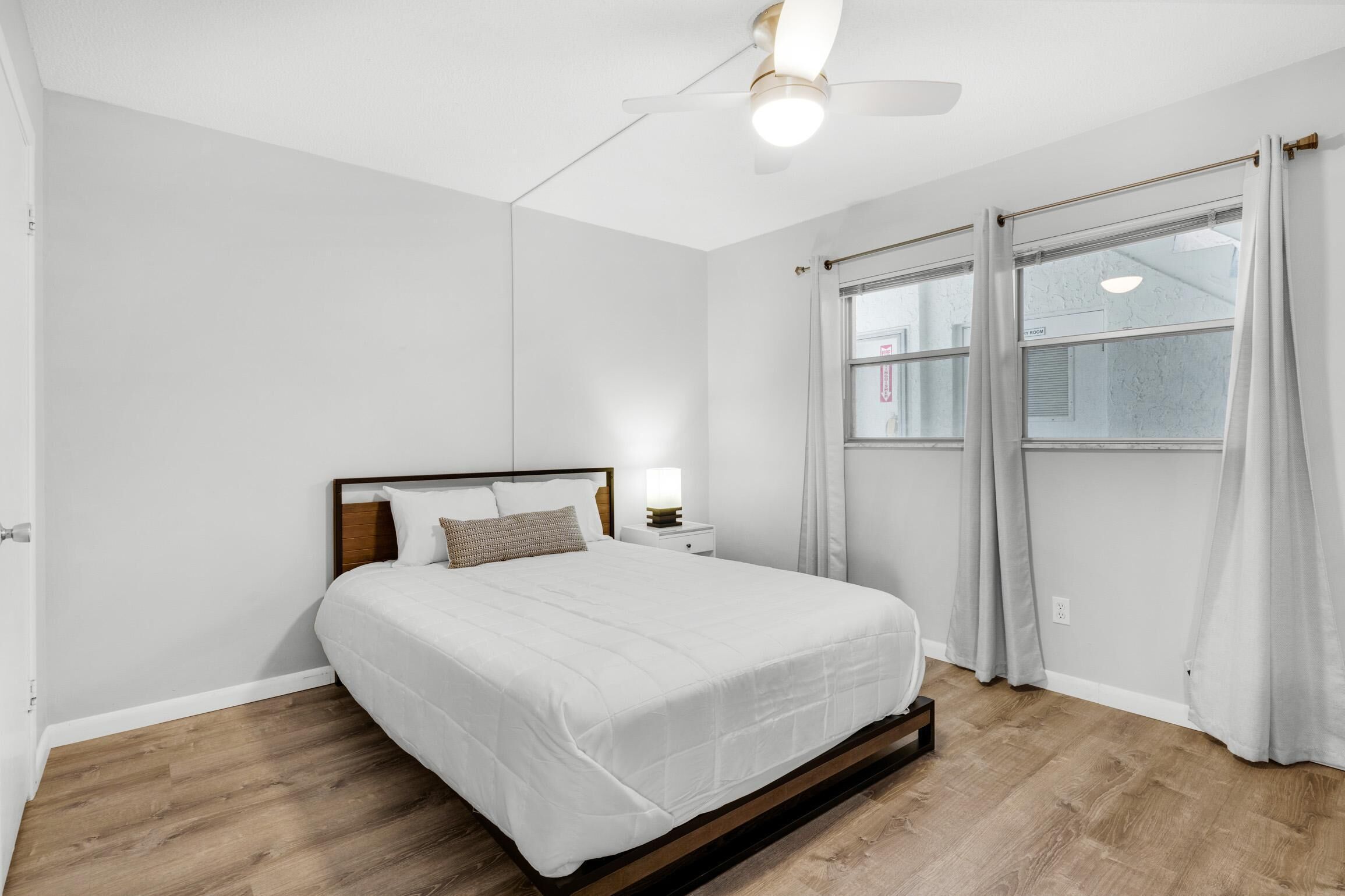 A bedroom with a bed, a nightstand, a ceiling fan, and a window with curtains.