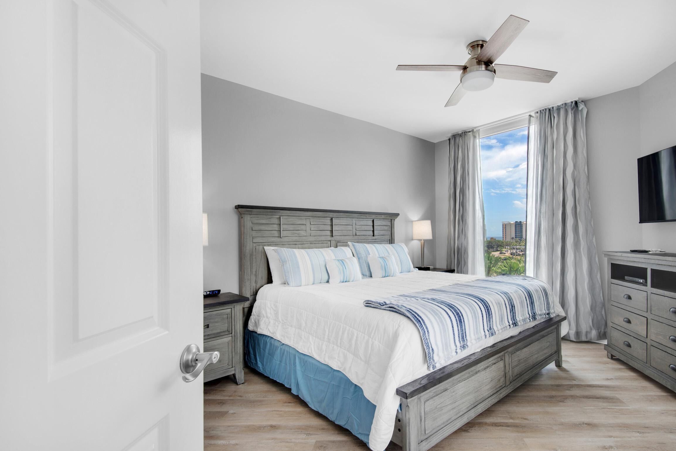 A bedroom with a bed, nightstands, a TV, and a window with curtains.