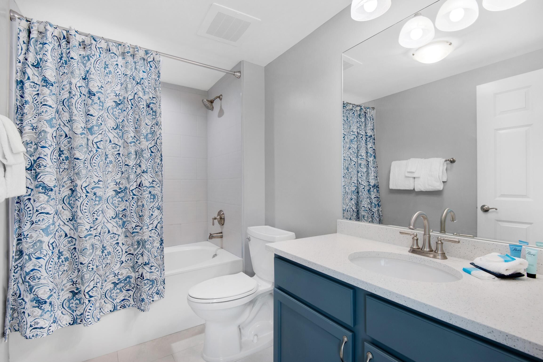 A bathroom with a shower curtain, toilet, bathtub, sink, and a mirror.