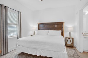 Ein Schlafzimmer mit einem großen Bett, einem Holzkopfende, zwei Nachttischlampen und einem Fenster mit Jalousien.