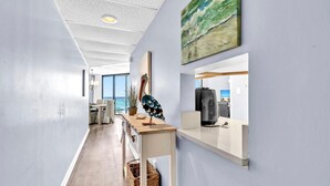 Ett modernt kontorsutrymme med en lång korridor, ett skrivbord i trä med en pelikanskulptur, en målning av vågor och utsikt över havet genom stora fönster.