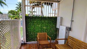 Uma área de pátio com mobiliário de madeira, uma parede verde e uma cerca branca.