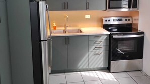 Uma cozinha compacta com armários cinza, geladeira de aço inoxidável, micro-ondas, forno e ventilador de teto.