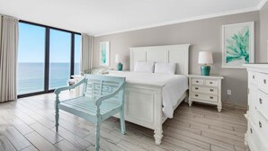 A bedroom with a large bed, a chair, a nightstand, and a dresser. - Edgewater Tower 3-1012 (Panama City Beach)