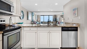 A modern kitchen with white cabinets, stainless steel appliances, and a granite countertop. - Edgewater Tower 3-1012 (Panama City Beach)
