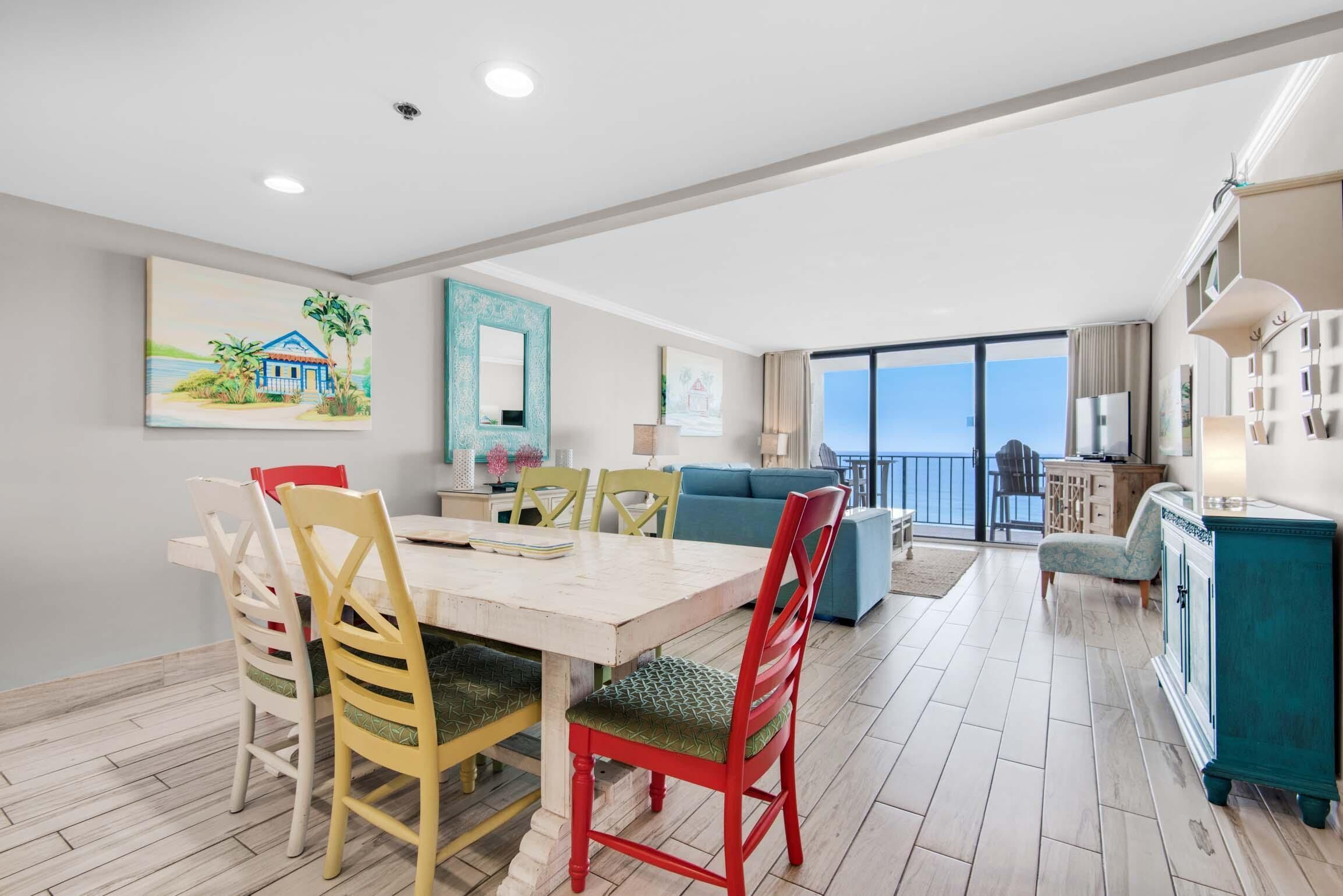 A dining area with a wooden table and chairs, a blue sofa, and a view of the ocean through large windows.