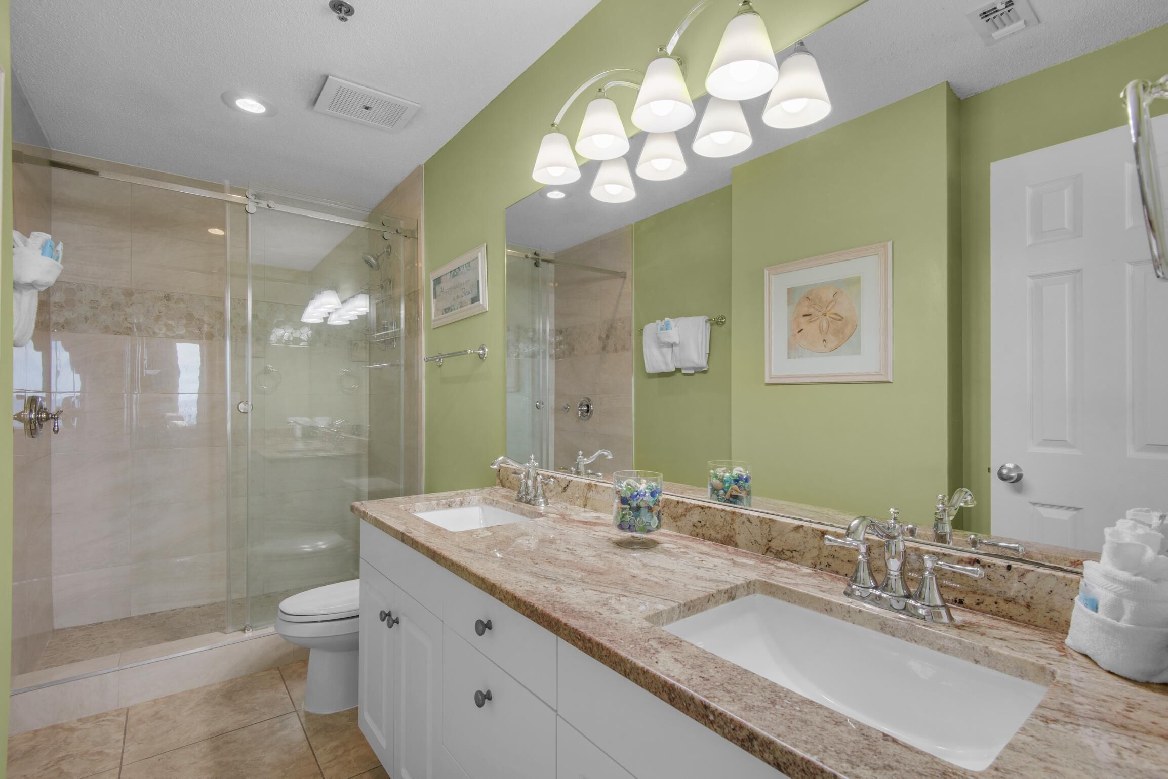 Une salle de bain dotée d’une douche à parois de verre, de deux vasques avec des plans de travail en marbre et d’un grand miroir.