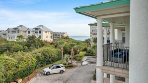 A residential area with multiple two-story houses, a white car parked on the street, and a view of the ocean. - Legacy 506- The Coastal Gem (Santa Rosa Beach)