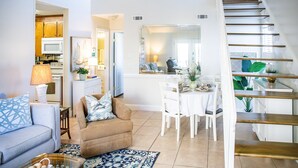 A living room with a sofa, a dining table with chairs, a staircase, and a kitchen area with cabinets and appliances. - Horizon South 38B (Panama City Beach)