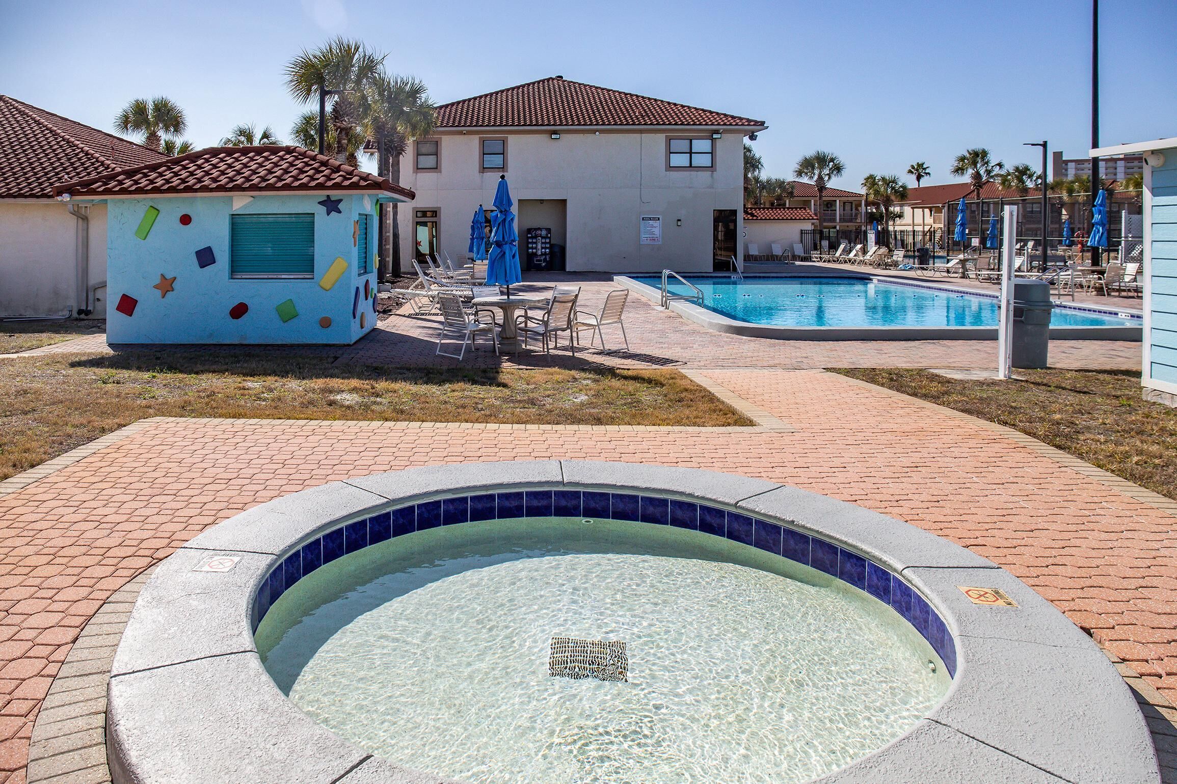 Un espace piscine comprenant un jacuzzi, des chaises longues et un petit bâtiment décoré de couleurs vives.